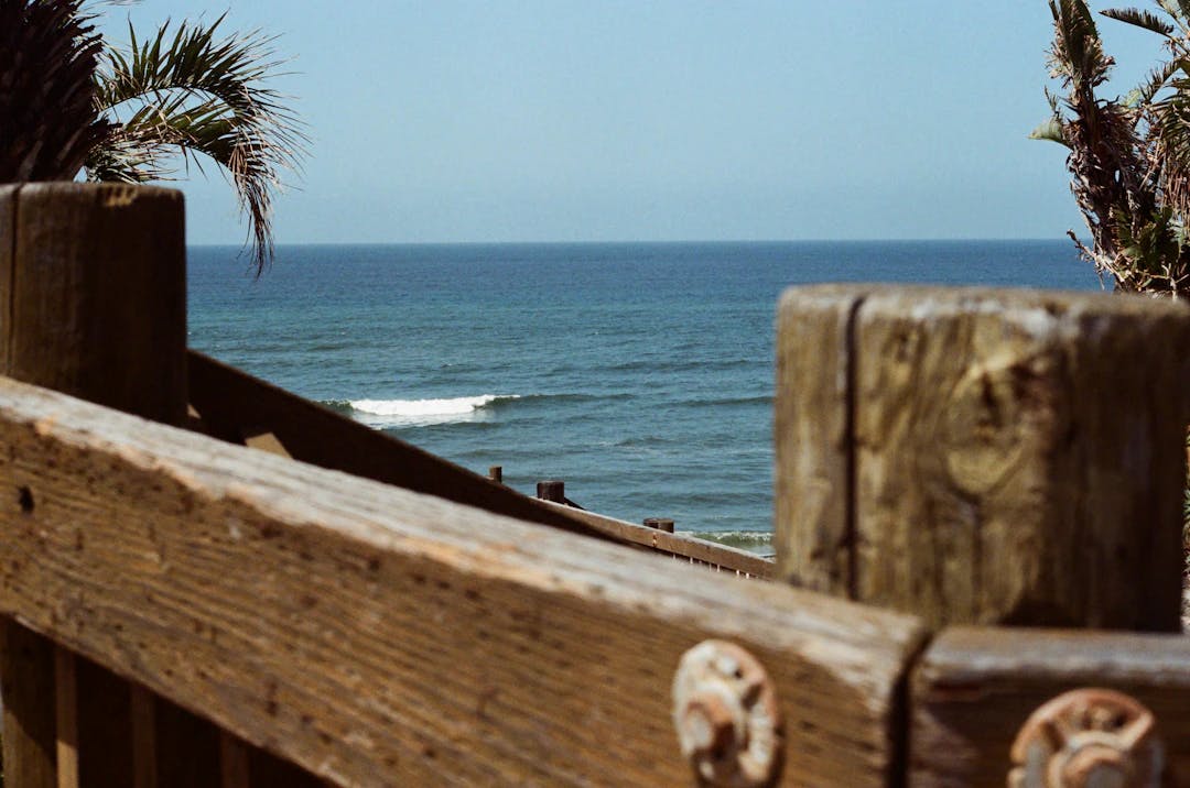 a view of the ocean from behind a wooden fence