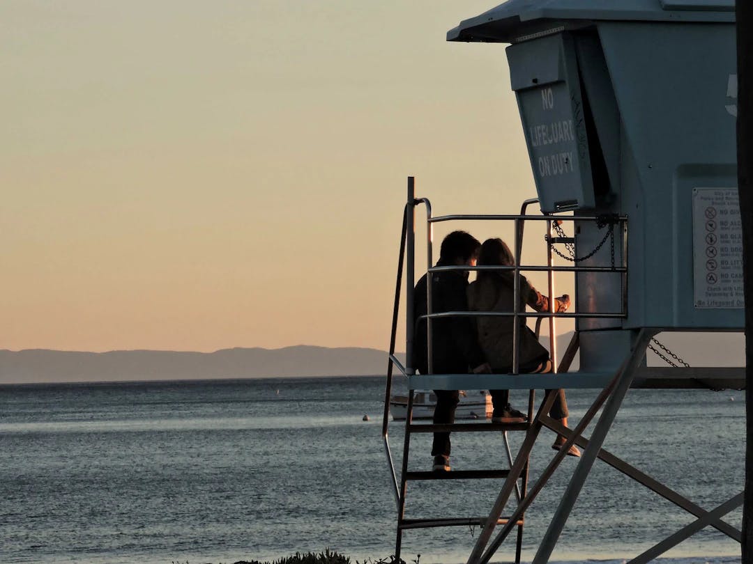 two people sitting on a lifeguard tower overlooking the ocean